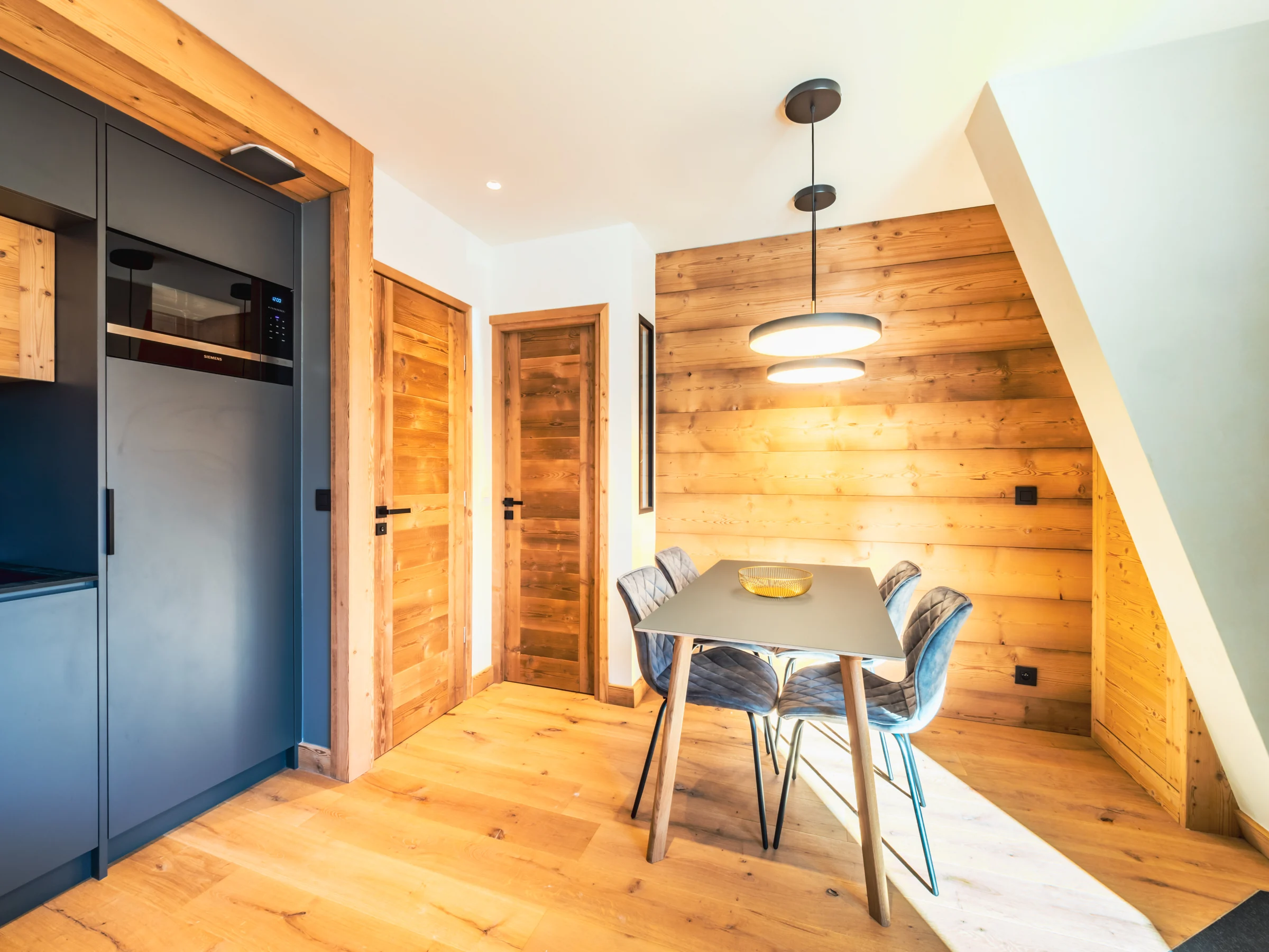Coin repas compact entre cuisine sombre, parquet clair et mur en bois.