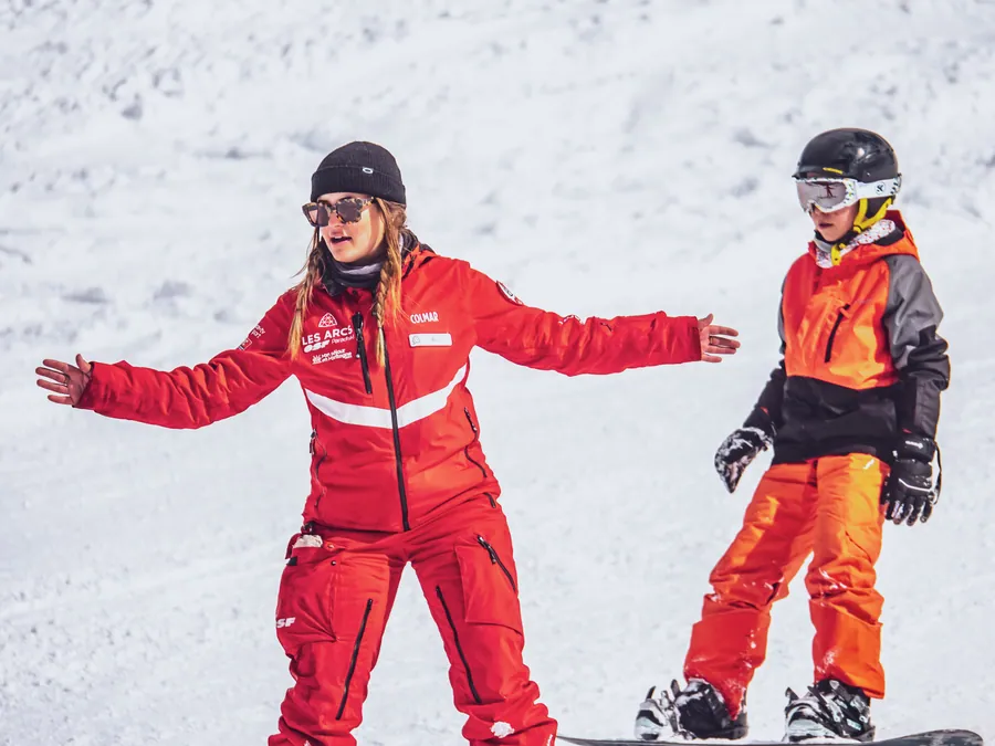 La monitrice explique le geste à un jeune snowboardeur