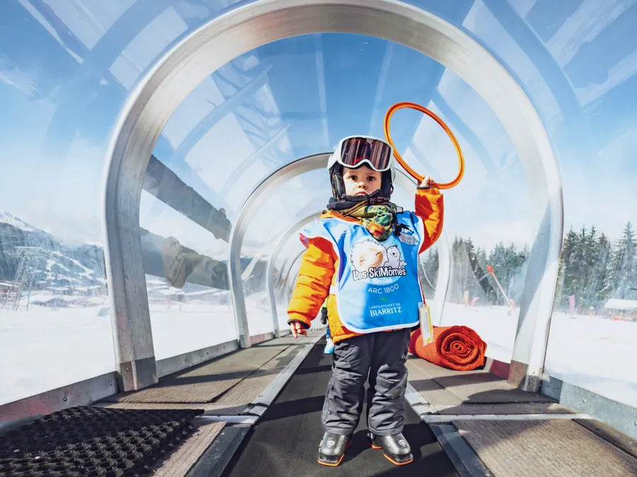 Un petit skieur et son cerceau dans le tunnel du tapis