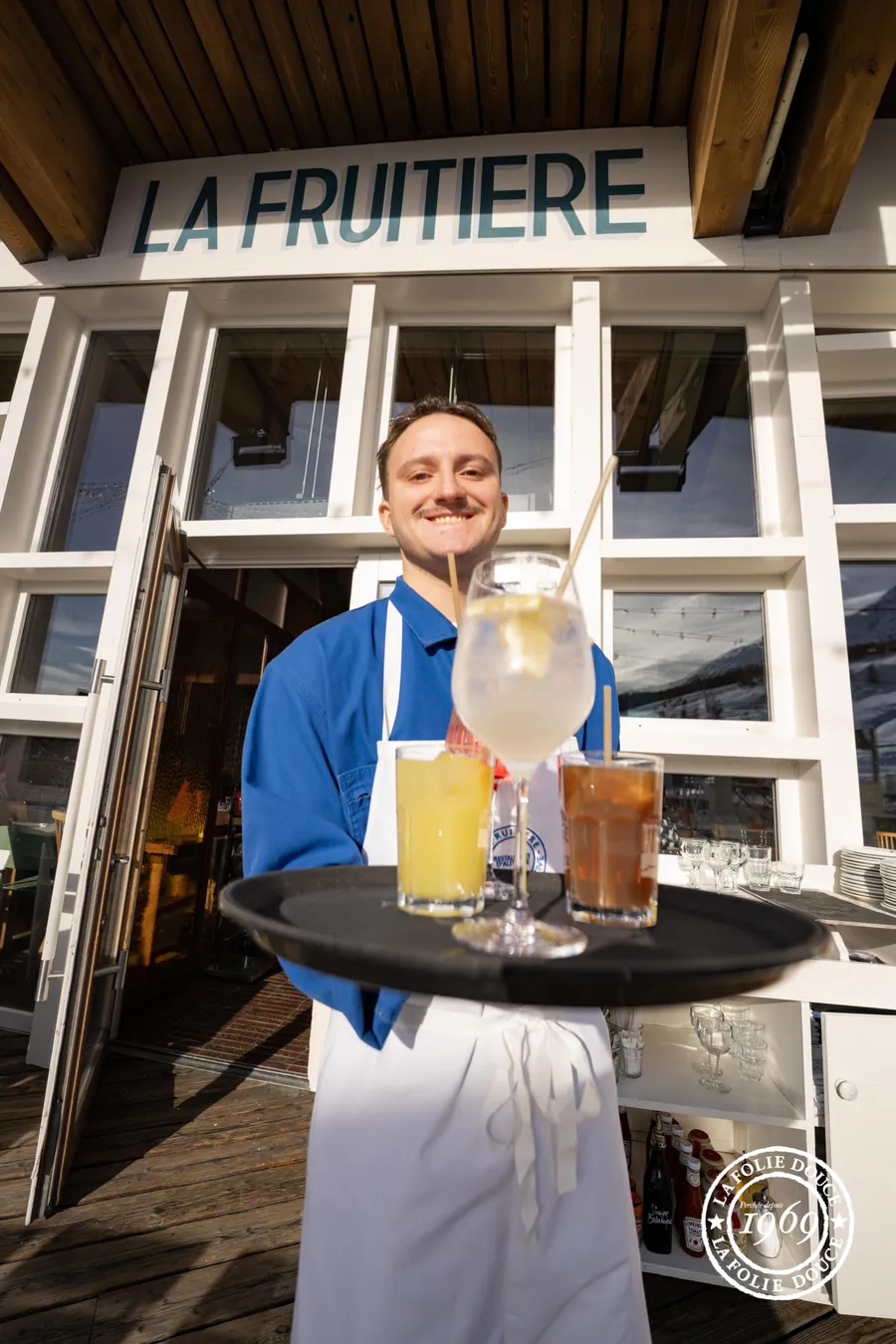 Une serveuse présente le plateau devant La Fruitière