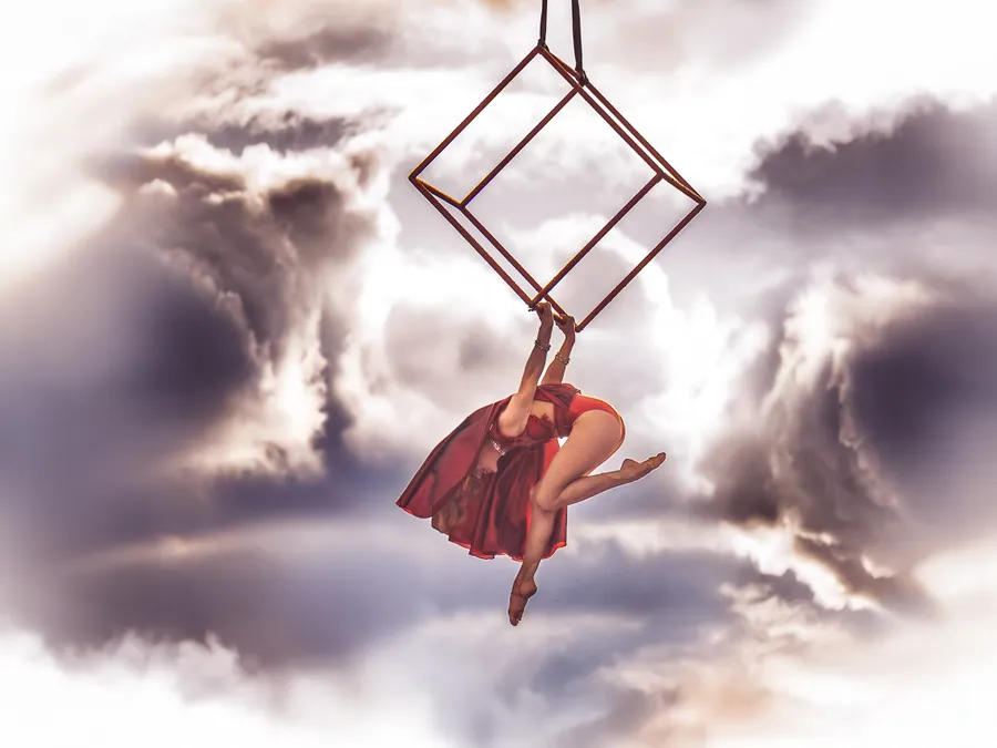 Une artiste suspendue à une structure aérienne devant les nuages