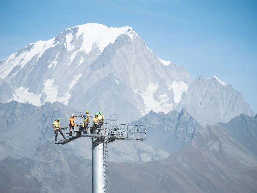 Des techniciens au sommet d’un pylône face au mont Blanc sur le chantier du Transarc